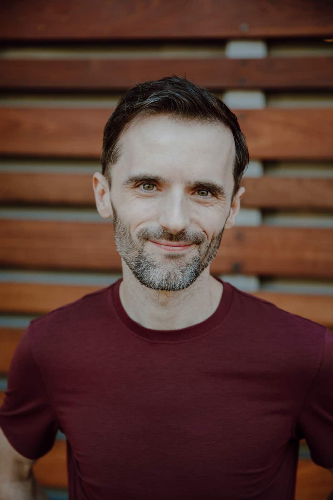 Michael standing in front of a warm wood-panneled wall smiling at the camera