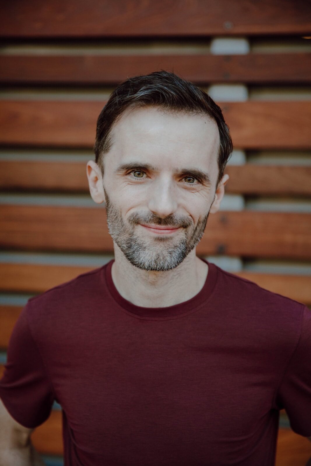 Michael smiling at viewer in front of a wall with wooden slats